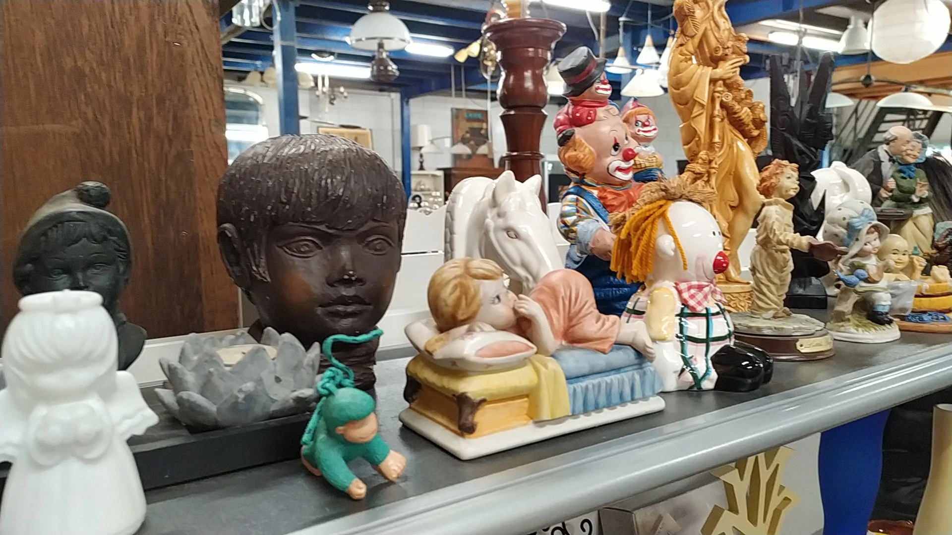 Vitrinekast met diverse beelden en decoratieve objecten zoals een bronzen gezicht, keramische figuren en gouden standbeelden