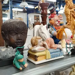 Vitrinekast met diverse beelden en decoratieve objecten zoals een bronzen gezicht, keramische figuren en gouden standbeelden
