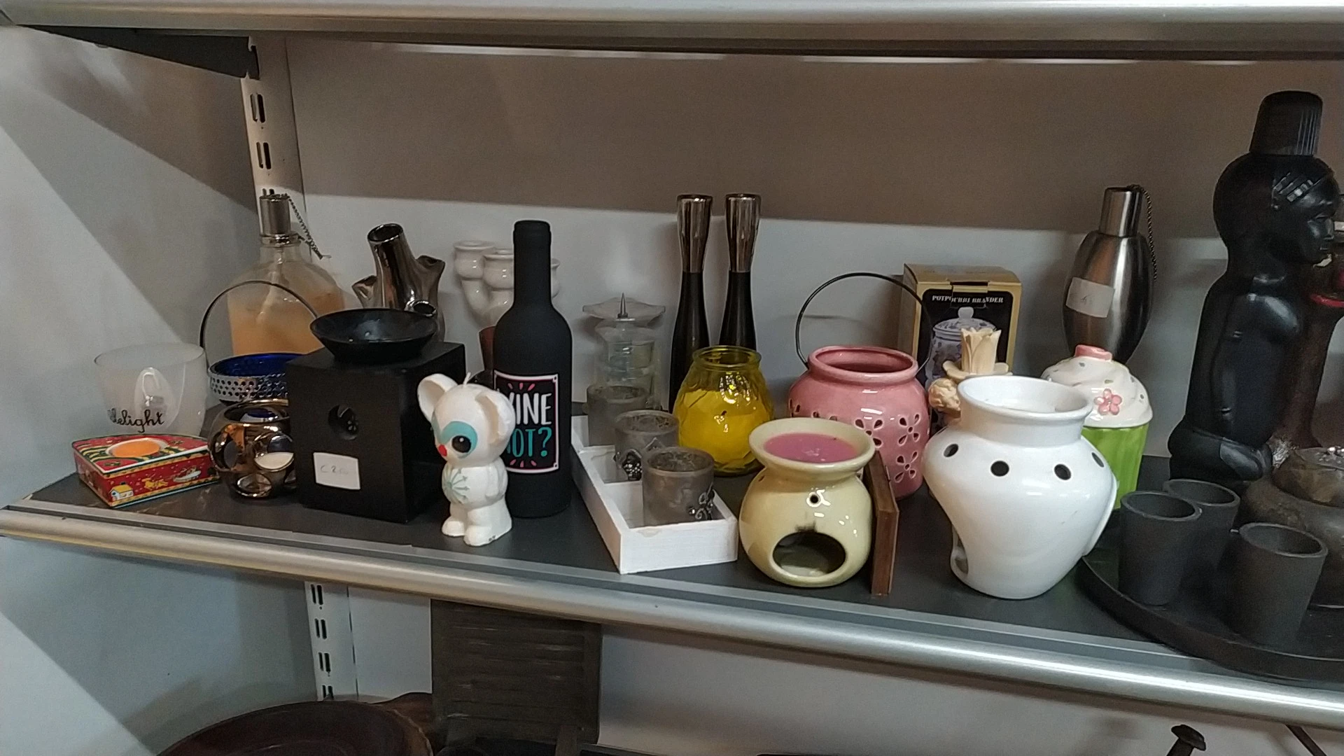 Stellingkast met diverse huishoudelijke items: flessen, decoratieve bekers, waxinelichthouders en een keramische dier figuur.
