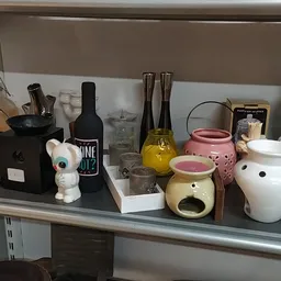 Stellingkast met diverse huishoudelijke items: flessen, decoratieve bekers, waxinelichthouders en een keramische dier figuur.