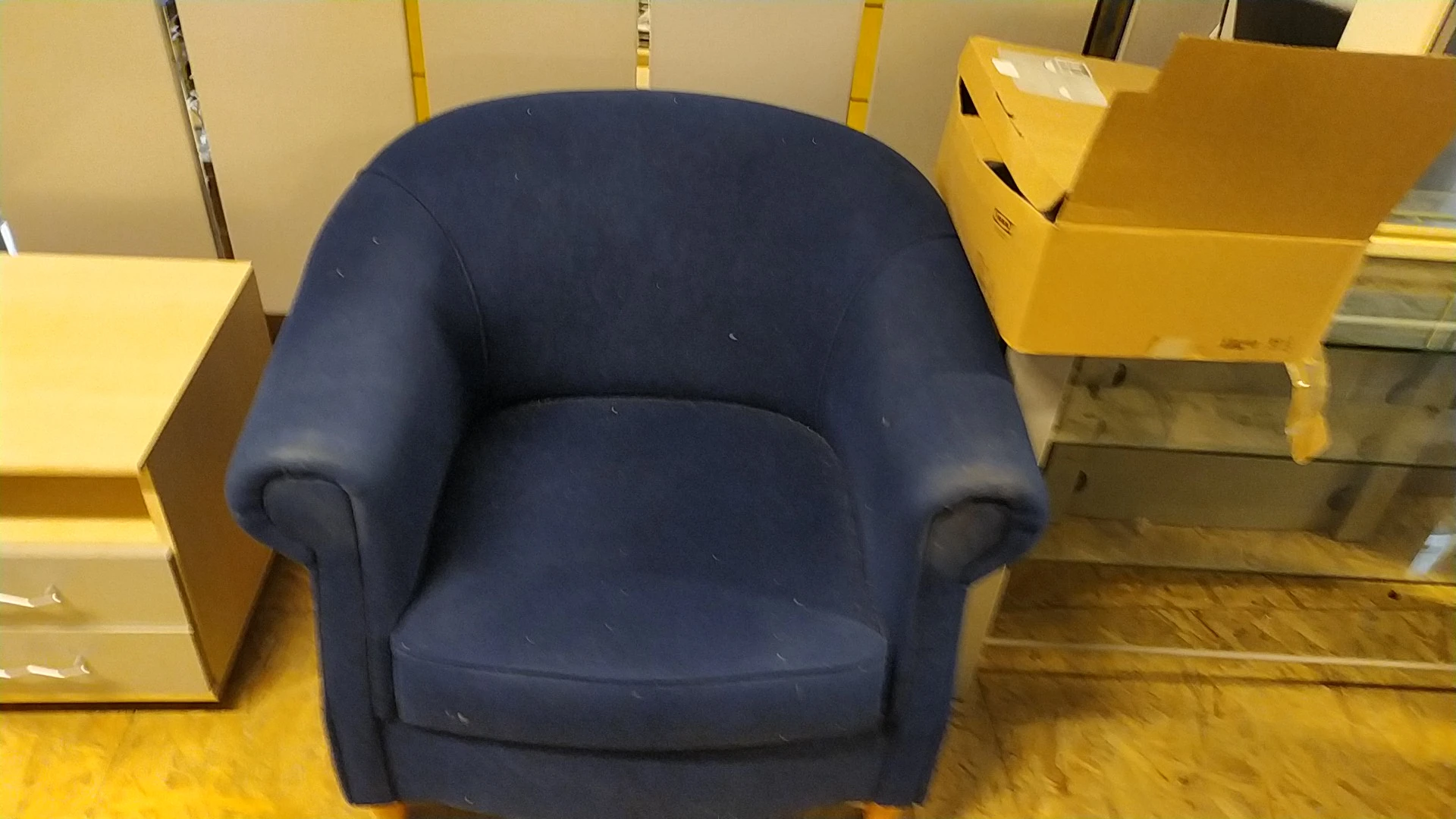 Blauwe fauteuil met ronde vormen en armsteunen in een kringloopwinkel.