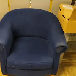 Blauwe fauteuil met ronde vormen en armsteunen in een kringloopwinkel.
