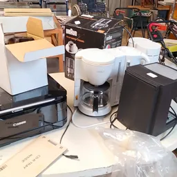 Verzameling tweedehands elektrische huishoudapparatuur: koffiezetapparaat, printer en andere elektronische apparaten op werkb