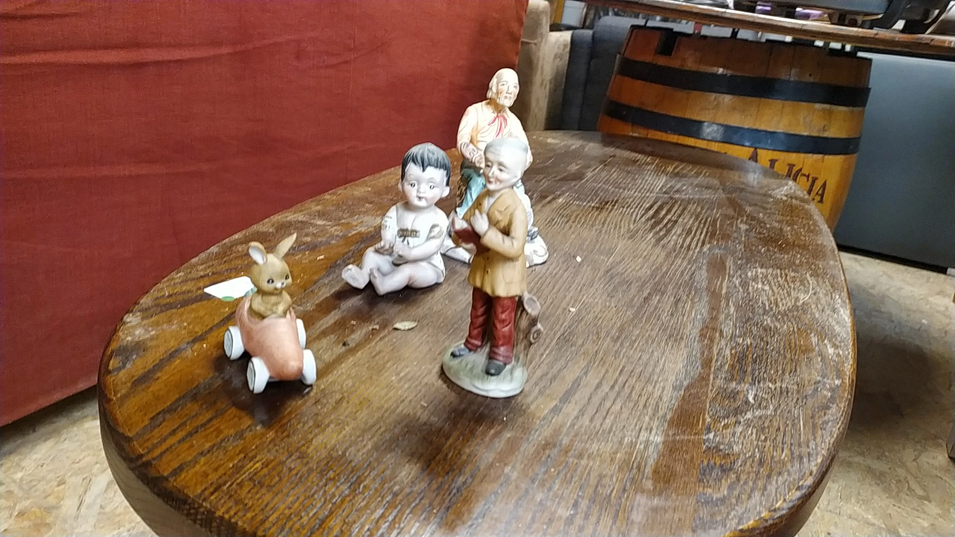 Vier vintage porseleinen figuurtjes op een houten tafel: een konijn in roze jurk, een zittend kind, een staand kind en een vr