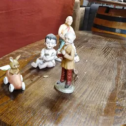 Vier vintage porseleinen figuurtjes op een houten tafel: een konijn in roze jurk, een zittend kind, een staand kind en een vr