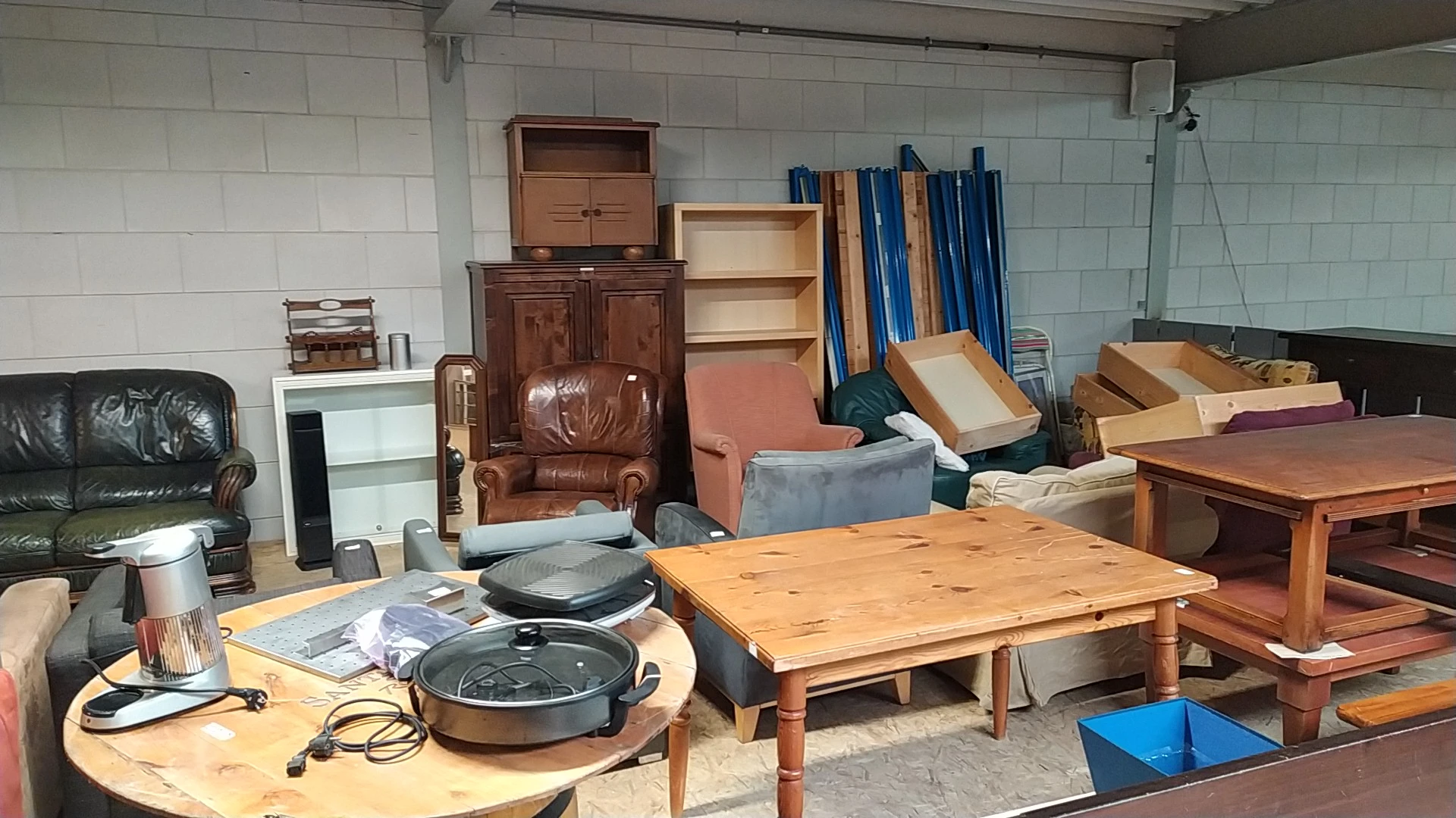 Tweedehands meubels in een kringloopwinkel: tafels, kasten, stoelen en huishoudapparatuur.