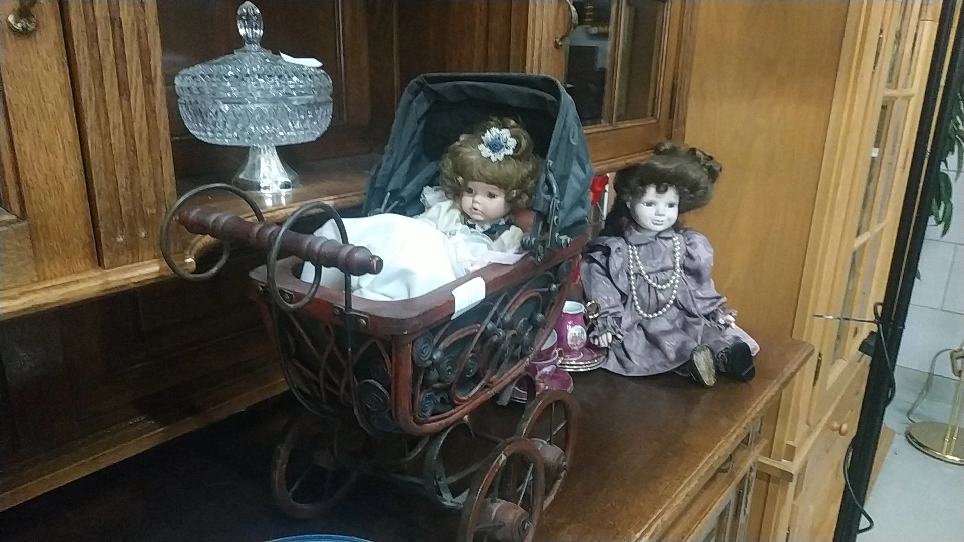 Antieke poppen en een houten kinderwagen met kristalglazen accessoires op een houten plank