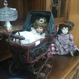 Antieke poppen en een houten kinderwagen met kristalglazen accessoires op een houten plank