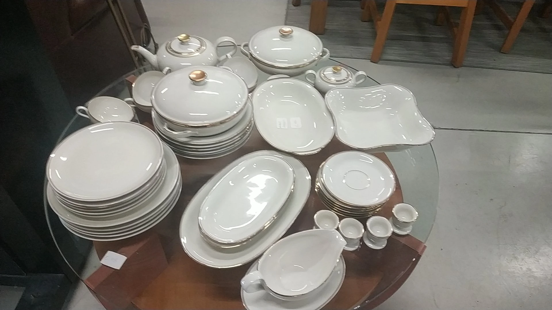 Verzameling wit servies met gouden rand, waaronder borden, schalen, terrine en kopjes op bruine tafel