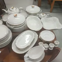Verzameling wit servies met gouden rand, waaronder borden, schalen, terrine en kopjes op bruine tafel
