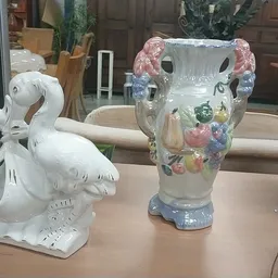 Twee decoratieve vazen op een tafel: een witte zwaan en een grijze vaas met bloemenopdruk