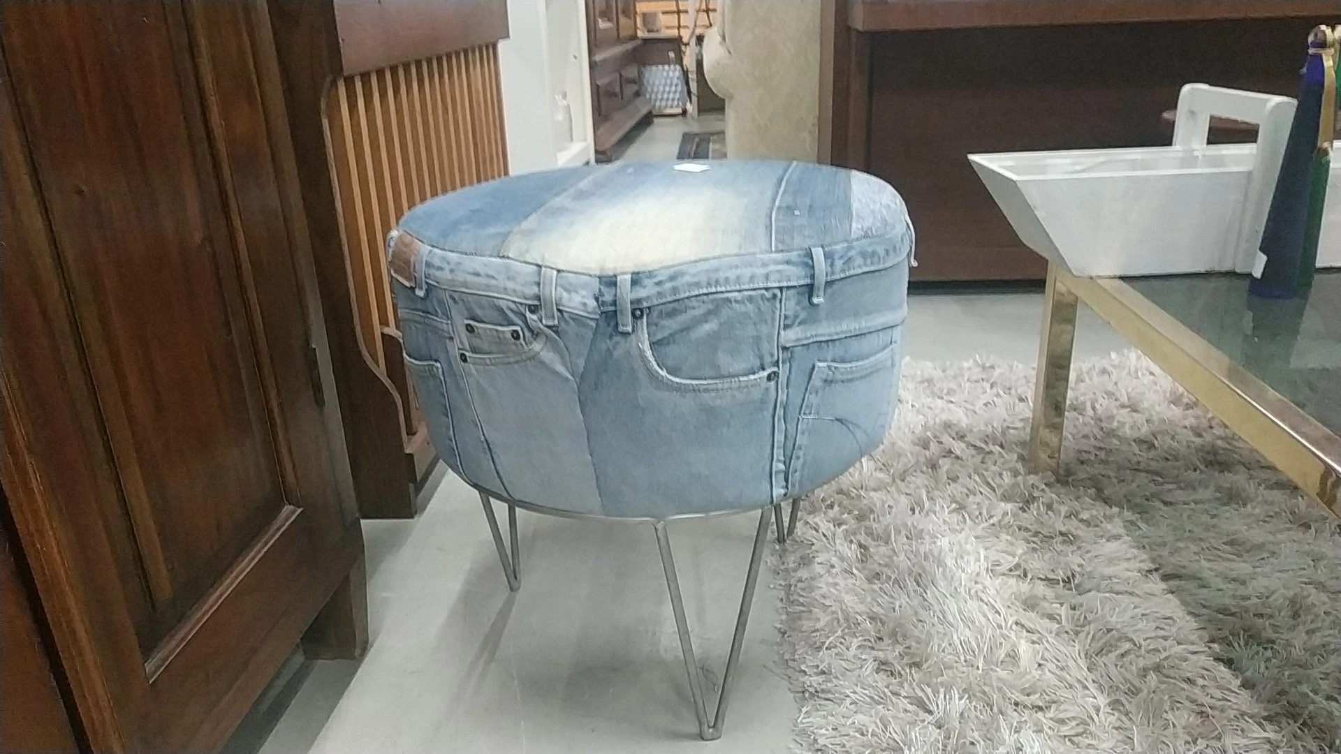 Ronde poef of tafel gemaakt van een uitgeholde jeansstof op metalen poten, opgesteld in een winkelvloer