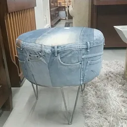 Ronde poef of tafel gemaakt van een uitgeholde jeansstof op metalen poten, opgesteld in een winkelvloer