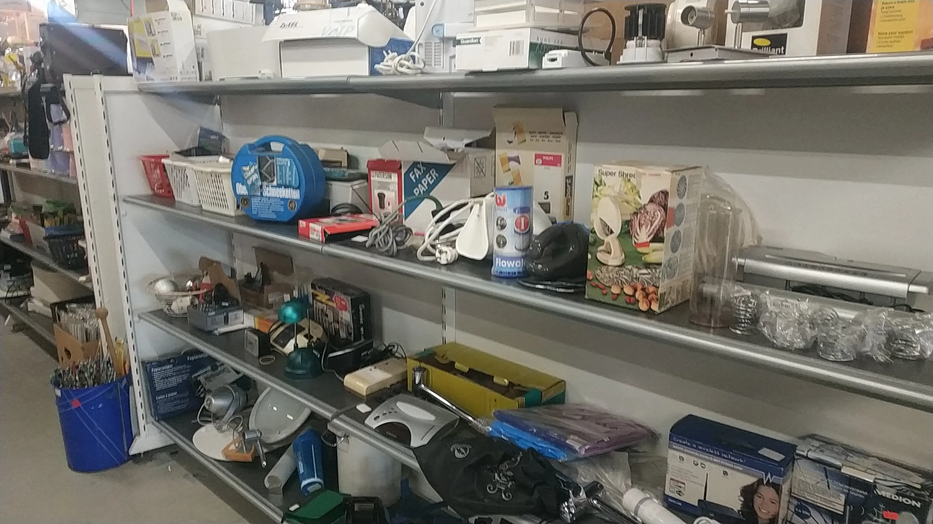 Metalen stellingen vol met diverse huishoudelijke artikelen, elektronische apparaten en kantoorspullen