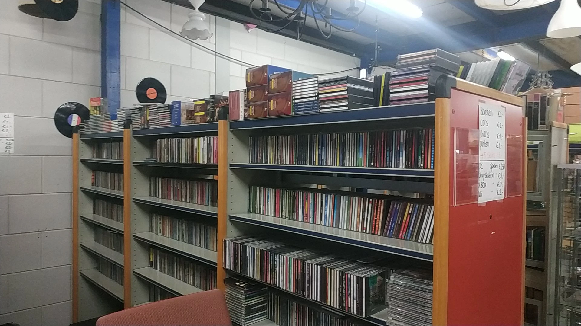 Stellingen vol met cd's en dvd's, georganiseerd op zwarte en gele kasten in een kringloopwinkel