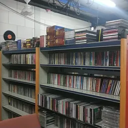 Stellingen vol met cd's en dvd's, georganiseerd op zwarte en gele kasten in een kringloopwinkel