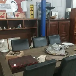 Winkelinterieur met houten meubels, vitrinekast, eettafel met stoelen en diverse huishoudelijke spullen op display