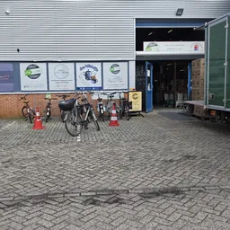 Voorzijde kringloopwinkel met bakstenen muur, uithangborden, fietsen en groene aanhanger