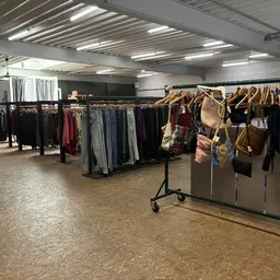 Winkelvloer met kledingrekken vol tweedehands kleding en accessoires, verlicht plafond