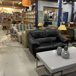 Winkelvloer met meubels: zwarte lederen bank, grijsblauwe stoelen, witte tafel, boekenrek op achtergrond