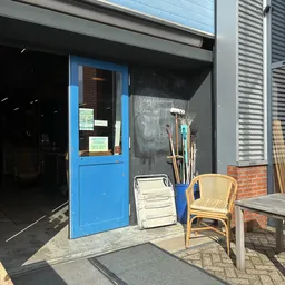 Ingang van kringloopwinkel met blauwe deur en uitgestalde spullen op het terras