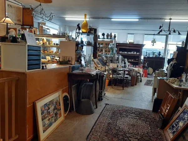 Binnenaanzicht van kringloopwinkel met toonbank, stellingen vol spullen, meubels, lampen en diversen
