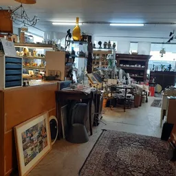 Binnenaanzicht van kringloopwinkel met toonbank, stellingen vol spullen, meubels, lampen en diversen