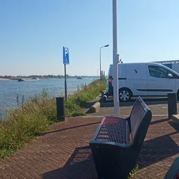 Parkeerplaats langs water met witte bestelwagen, parkeerbordje en houten bankje