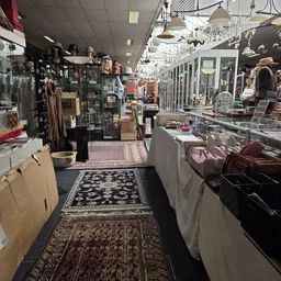 Binnenaanzicht van kringloopwinkel met kledingrekken, vitrines, tafels met spullen en kasten langs de wanden