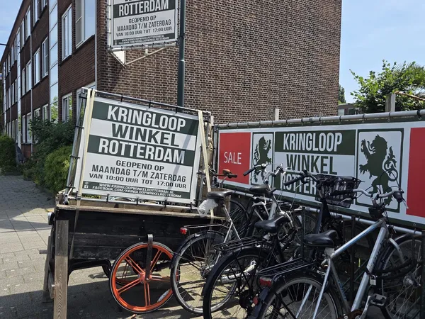 Voorgevel van kringloopwinkel met etalage, fietsen geparkeerd ervoor en reclameborden