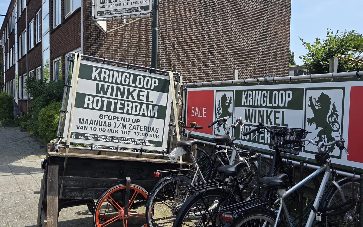 Voorgevel van kringloopwinkel met etalage, fietsen geparkeerd ervoor en reclameborden