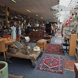 Winkelvloer van kringloopwinkel met diverse meubels, kleding op hangers, boeken en huishoudartikelen