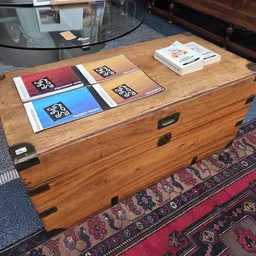 Houten antieke koffer met daarop geordende boeken in verschillende kleuren op een bruine vloer