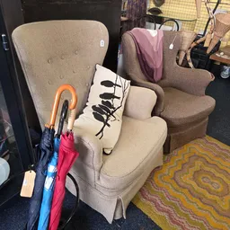 Bruine stoelen en fauteuils met kussens, paraplu's en otras huishoudartikelen in een kringloopwinkel