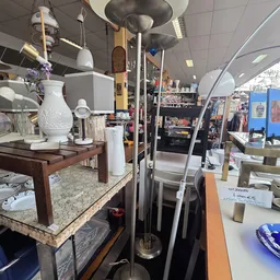 Winkelinterieur met vitrinekast bevat witte decoratieve objecten, lampen en huishoudelijke spullen op houten tafels
