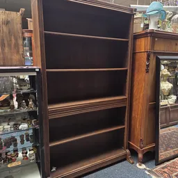 Houten boekenkast met donkere achterwand en meerdere legplanken, geflankeerd door twee andere meubels