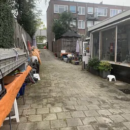 Binnenplaats met paden tussen kringloopspullen, stellingen en opslag aan weerszijden