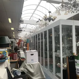 Winkelinterieur met glazen vitrines, hangende lampen en diverse tweedehands spullen onder een glazen plafond