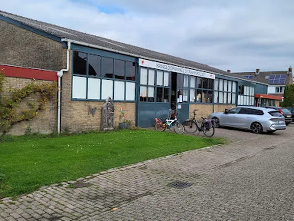 Voorgevel van kringloopwinkel met grijze kozijnen, bakstenen muur en parkeerplaats met fietsen