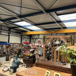 Ruim kringloopwinkelinterieur met stellingen vol spullen, houten toonbank op voorgrond, gele hijskraan aan plafond, daglicht 