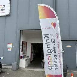 Grijze gevel met open deur en groot wit spandoek met kleurrijke afbeelding en tekst