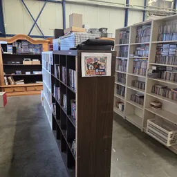 Binnenkant kringloopwinkel met boekenkasten, CD-rekken en diverse stellingen vol met tweedehands spullen