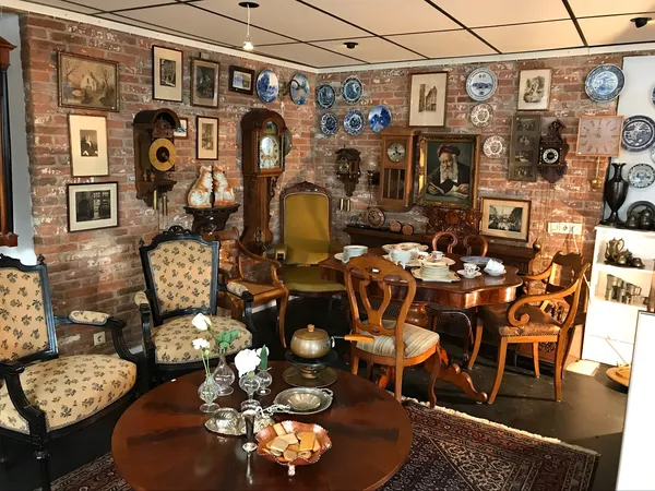 Ingerichte woonkamer met antieke meubels, schilderijen en decoratiestukken aan bakstenen muur