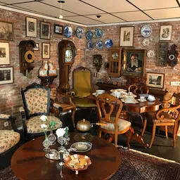 Ingerichte woonkamer met antieke meubels, schilderijen en decoratiestukken aan bakstenen muur