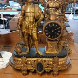 Gouden decoratief mantelklok met beeldhouwwerk van een figuur in klassieke stijl op zwart marmer voetstuk
