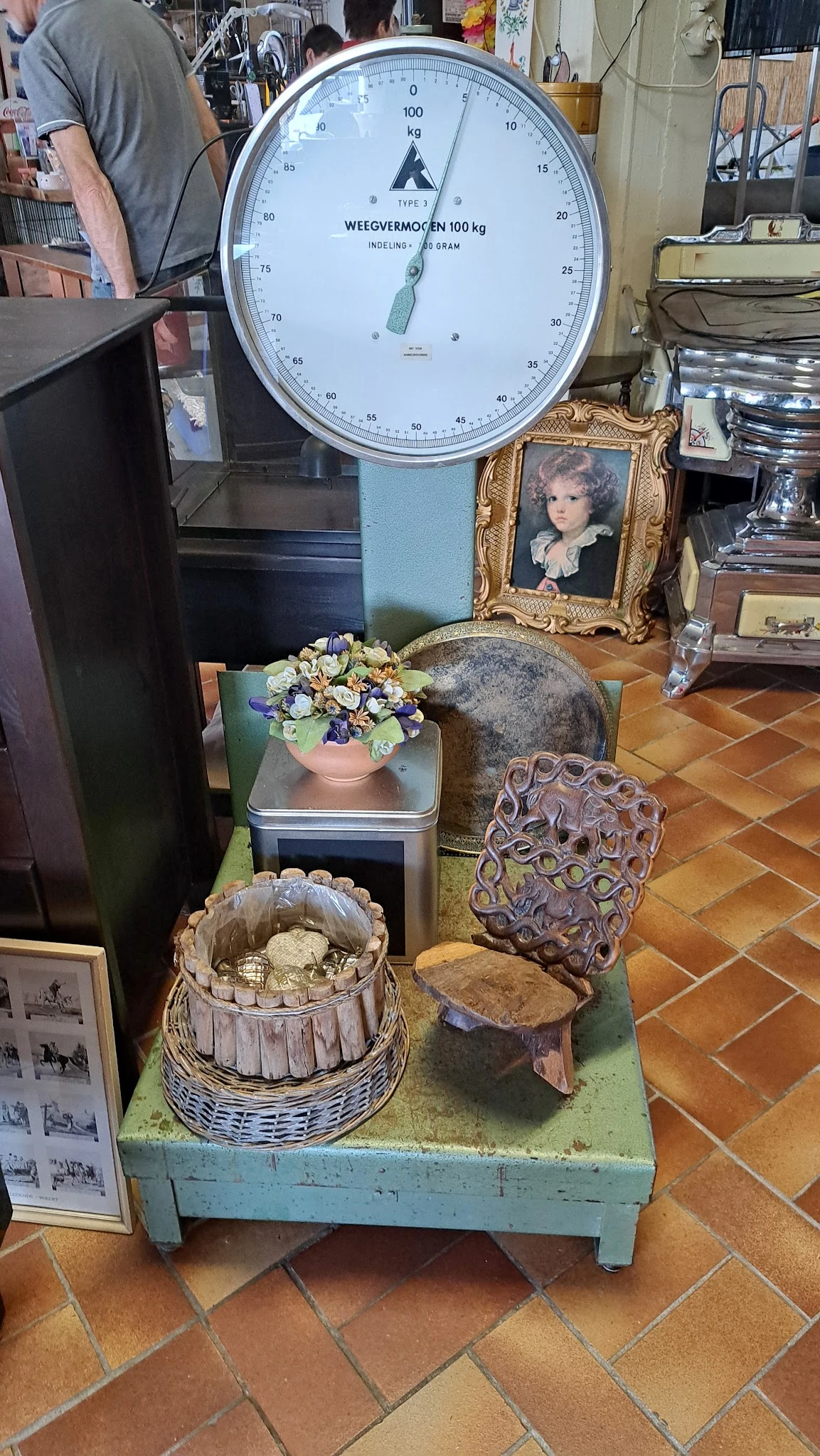 Diverse tweedehands voorwerpen: bloempot met kunstbloemen, houten stoel, decoratief beeld, oude weegschaal en andere huishoud
