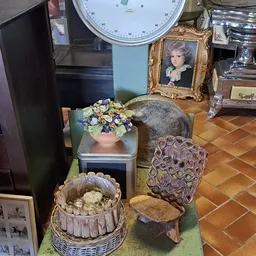 Diverse tweedehands voorwerpen: bloempot met kunstbloemen, houten stoel, decoratief beeld, oude weegschaal en andere huishoud