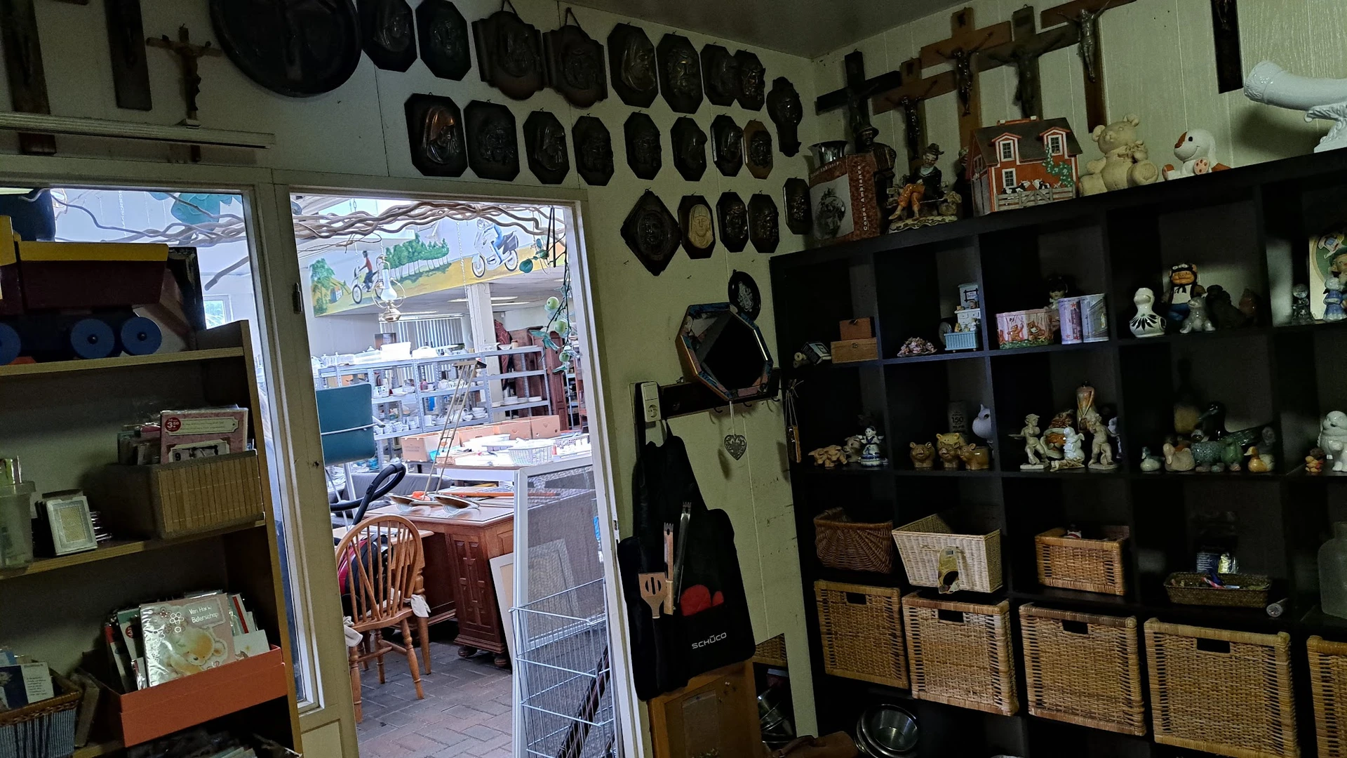 Winkelbinnenruimte met zwarte pannen aan muur, houten kruis, kasten met decoratieve items en rieten manden