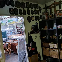 Winkelbinnenruimte met zwarte pannen aan muur, houten kruis, kasten met decoratieve items en rieten manden