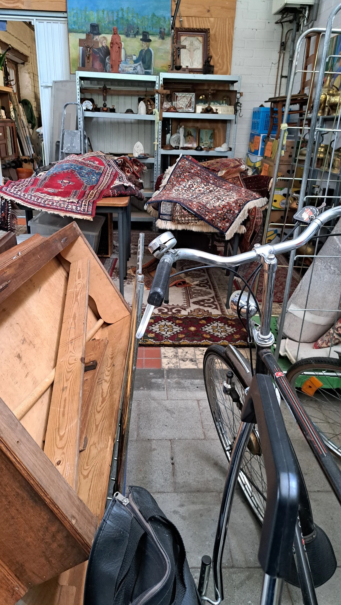 Verzameling tweedehands meubels en huishoudartikelen in een kringloopwinkel, waaronder een fiets, houten kastje, tapijten en 
